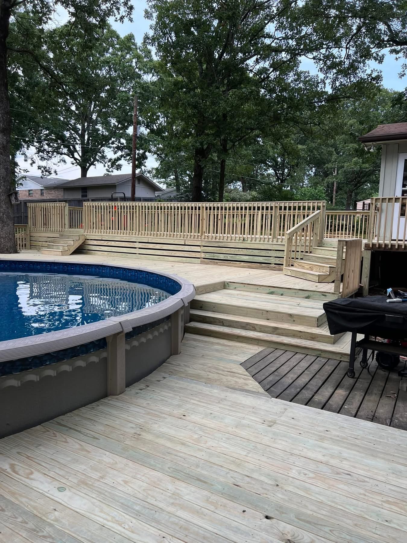 Custom wood deck wrapping an above-ground pool with railings and wide steps